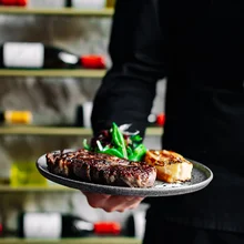 chef in black uniform holds plate of steak dinner