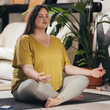 Adult woman sitting in a lotus pose with her eyes closed, relaxing and meditating. Health at any size.