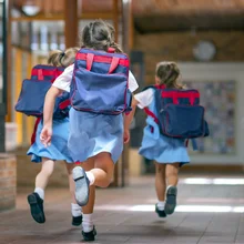 Rear view of excited students running towards entrance. Girls are carrying backpacks while leaving from school. Happy friends are wearing school uniforms.