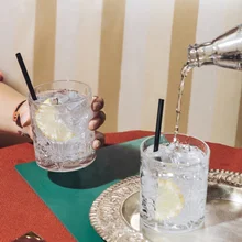 A girl holds a glass of gin and tonic while tonic water is poured, into an elegant pop-colored bar