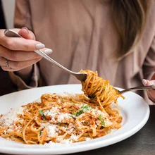 Girl eats Italian pasta with tomato, meat. Close-up spaghetti Bolognese wind it around a fork with a spoon. Parmesan cheese